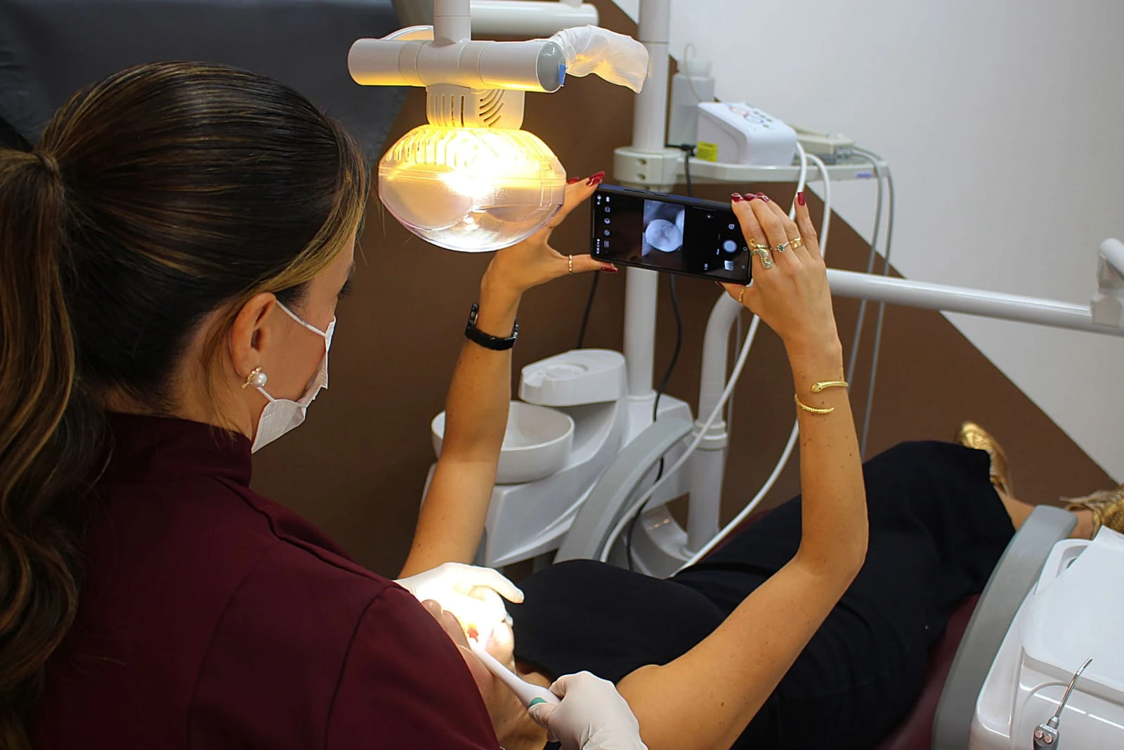 Dra. Andrea atendendo uma paciente, que acompanha pela tela do celular a imagem do próprio dente